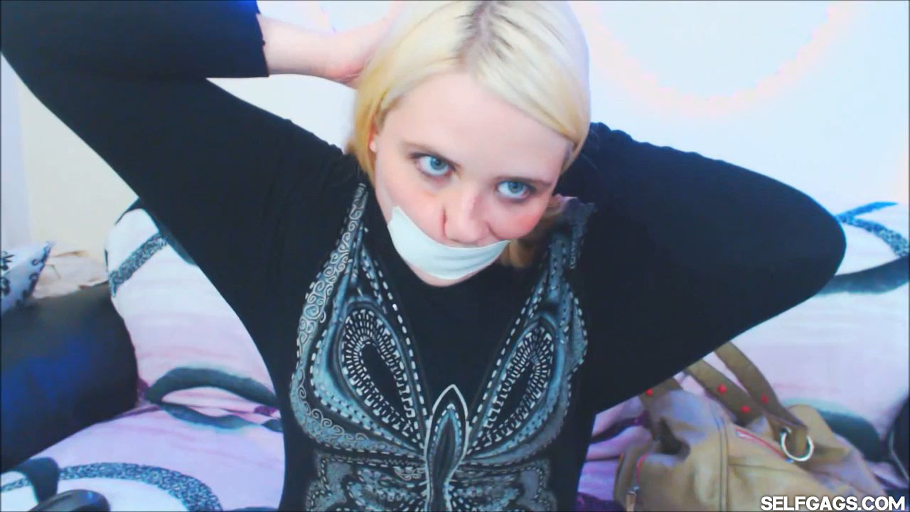 Blonde girl gags herself with microfoam tape around the head at selfgags.com