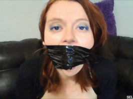 Redhead gagged with black bondage tape around the head