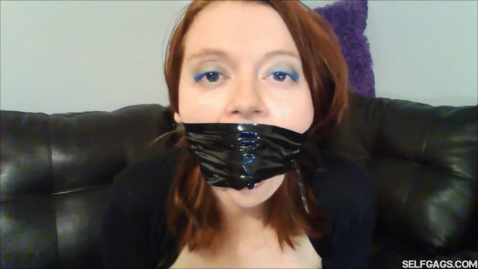 Redhead gagged with black bondage tape around the head