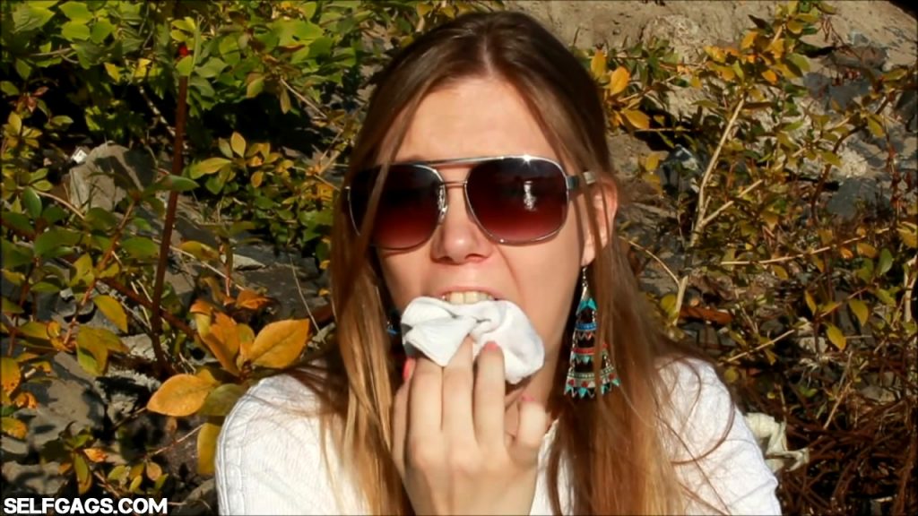 Girl with sunglasses stuffs dirty socks in her mouth