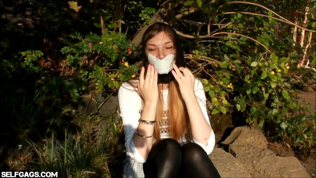 Tape gagged model head encased with fishnet pantyhose outdoors