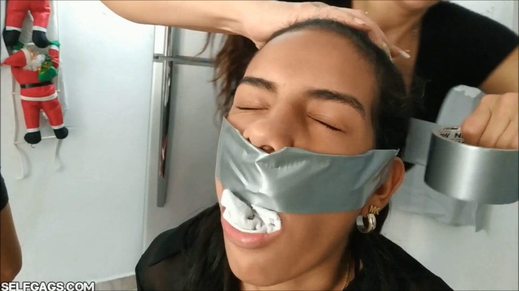 Young latina girl with socks in her mouth is getting gagged with silver duct tape wrapped around the head by powerful bdsm milf