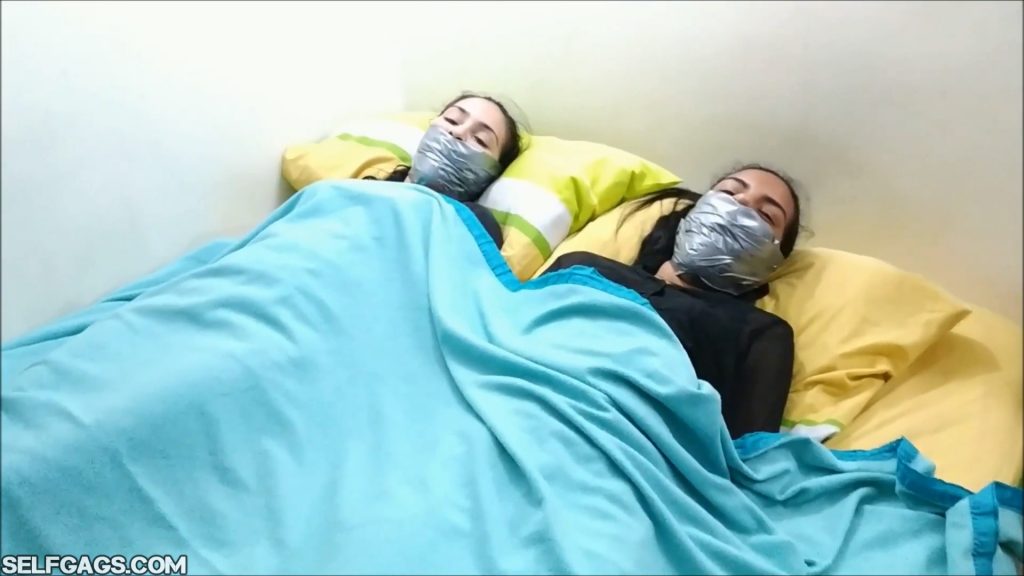 Two tied and tightly tape gagged latina sisters bound and gagged under a blanket in the bed