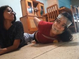 Gagged girl hogtied by girl with glasses in tight tape bondage