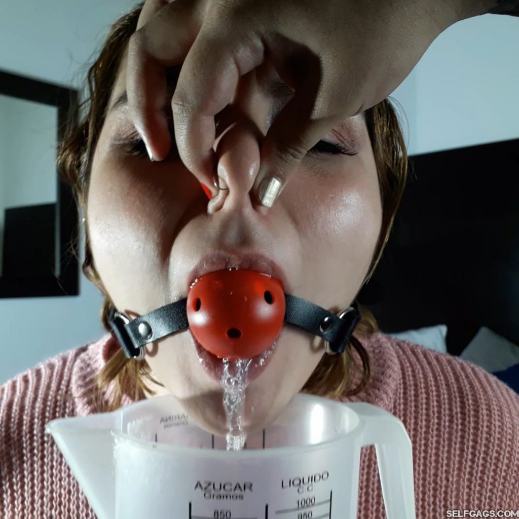 Drooling latina girl in woolen sweater has nose pinched shut while gagged with red ball gag
