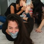 An angry hogtied woman gagged with duct tape has her bare feet licked by two lesbian girls