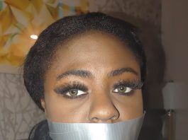 Black Beautiful Bitch In Rope Bondage – Ebony BDSM A black woman with green eyes is gagged with silver duct tape in a living room