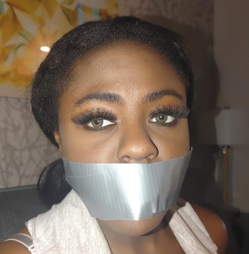 Black Beautiful Bitch In Rope Bondage – Ebony BDSM A black woman with green eyes is gagged with silver duct tape in a living room