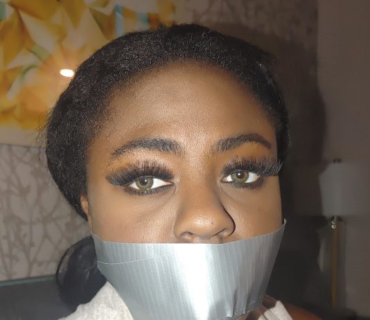 Black Beautiful Bitch In Rope Bondage – Ebony BDSM A black woman with green eyes is gagged with silver duct tape in a living room