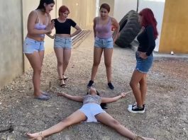 Young woman in outdoor bondage is tied spreadeagle on the ground by four dominant women