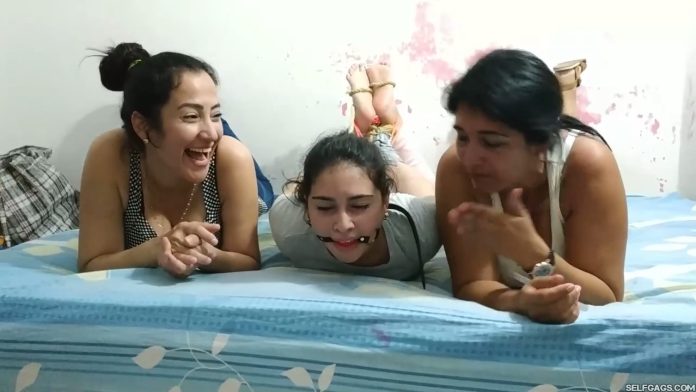 Barefoot girl hogtied and ball gagged by two women