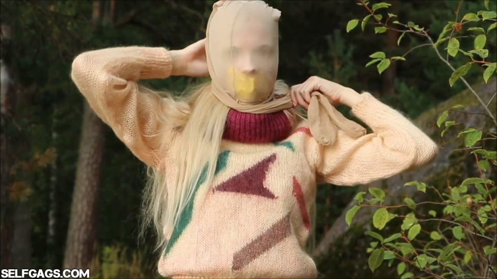 Blonde sweater girl self-gagged in forest