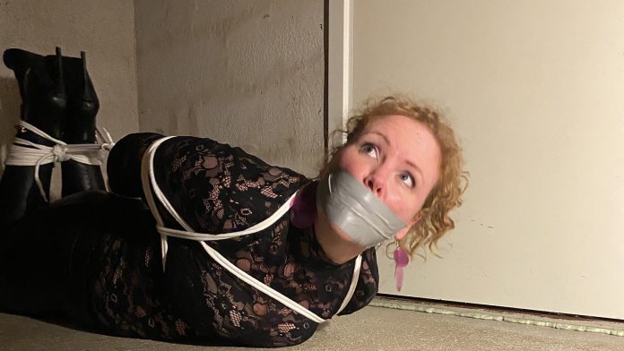 Hogtied party girl gagged with tape on basement room floor