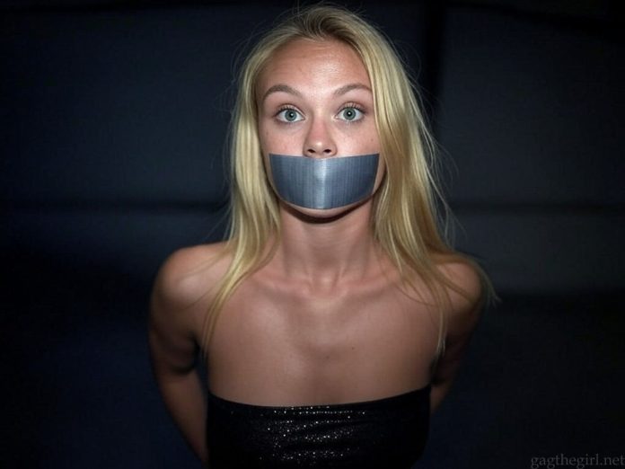 Blonde Danish event girl named Asta, duct tape gagged and bound, wearing a black glittering top, wide-eyed and staring fearfully in a dark setting.