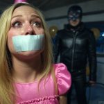 An 18-year-old birthday girl in a pink dress and party hat, duct tape gagged with tears streaming. A leather-clad sadist with a whip looms ominously.