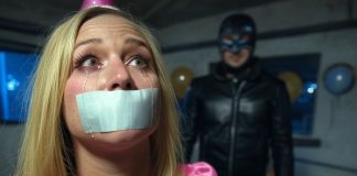 Terrified Birthday Girl Gagged, Facing Sadistic Punishment An 18-year-old birthday girl in a pink dress and party hat, duct tape gagged with tears streaming. A leather-clad sadist with a whip looms ominously.