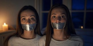 Two Brunette Sisters Tape Gagged in Candlelit Bedroom Two brunette sisters, around 19 years old, tape gagged and tied, sitting on a bed in a candlelit bedroom, gazing at the viewer with seductive expressions.