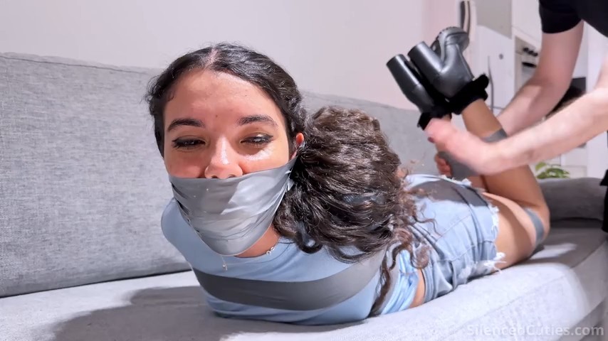 Addy moaning with cheeks puffed under layers of wrapped tape