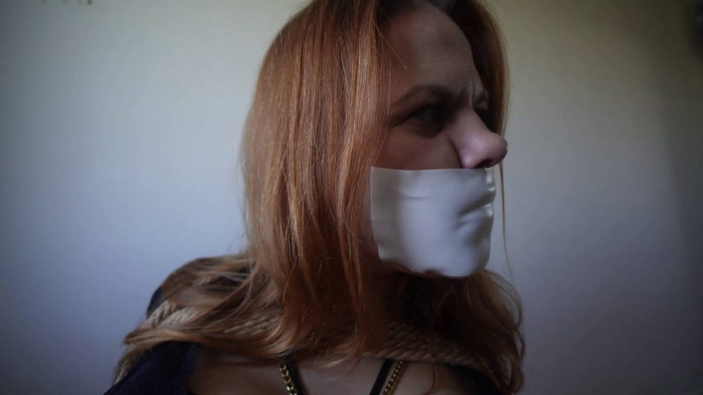Close-up of June’s tightly taped mouth with microfoam gag asfrom the side