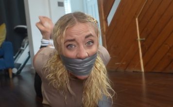 Zoey’s gagged face in close-up, duct tape pressing over bulging sock gag