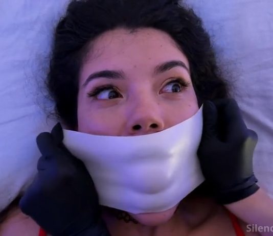 Addy Rosse Jawbreaker Ball Gagged & Tape Wrapped Birthday Surprise – Silenced Cuties Addy Rosse wide-eyed as gloved hands press white microfoam tape tightly over her mouth during birthday bondage surprise – Silenced Cuties