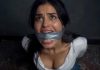 Brunette Duct Tape Cleave Gagged & Struggling Helplessly on Floor – AI Bondage Woman with duct tape over her mouth, looking upward with a distressed expression in a dim room.