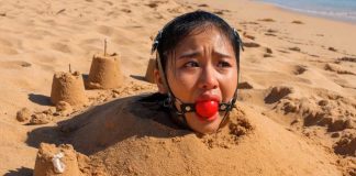 Close up of terrified Southeast Asian beauty with thick harness ball gag strapped in her mouth, eyes wide with fear