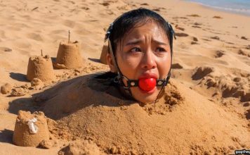 Southeast Asian Harness Ballgagged & Bucket Hooded on Beach – AI Bondage Close up of terrified Southeast Asian beauty with thick harness ball gag strapped in her mouth, eyes wide with fear
