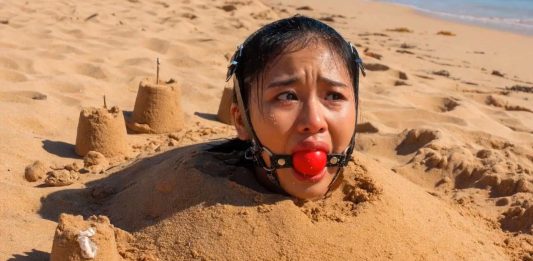 Southeast Asian Harness Ballgagged & Bucket Hooded on Beach – AI Bondage Close up of terrified Southeast Asian beauty with thick harness ball gag strapped in her mouth, eyes wide with fear