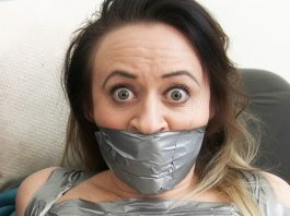Why Men Find Tape-Gagged Women So Attractive Brunette woman with wide eyes tightly gagged with multiple layers of silver duct tape covering her mouth and lower face