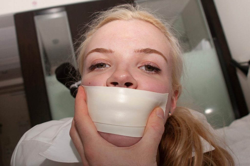 Gagged woman with white microfoam tape over her mouth, a hand holding her face