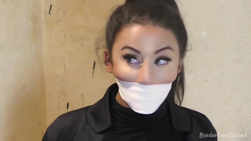 Bella OTM extreme CU — white wrap tight across mouth, eyes cutting aside against plain wall