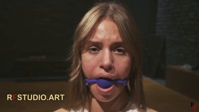 Lali's face in a blue ball gag, looking straight into the camera