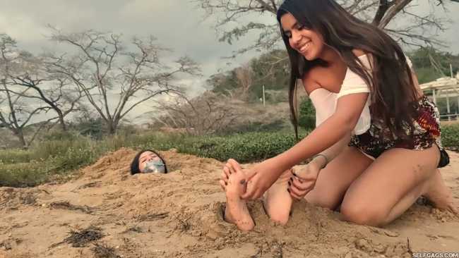 Sand buried girl has feet tickled
