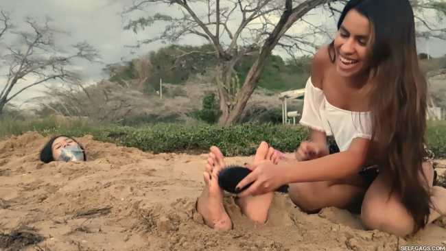 Sand buried girl has feet tickled