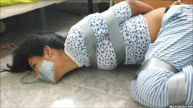 A gagged girl in tape bondage is struggling in order to escape her bondage. She is wearing a pajamas and is barefoot while bound and gagged
