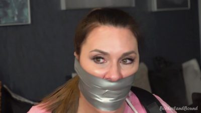 Eliza tape CU — multi-wrap silver duct tape seals Eliza’s mouth; pink tee and black harness strap in soft BG