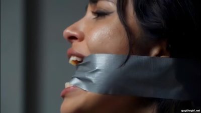 Close-up profile of brunette woman with thick silver duct tape cleave gag forced between her teeth, sweat glistening on her face
