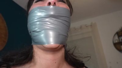 Tight face close-up of the duct-tape OTM gag, tears in her eyes