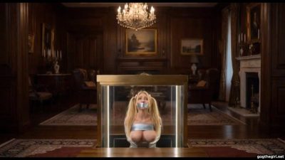Wide shot of the glass display case lowering with bound and gagged teacher Julie Millard inside opulent room