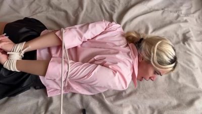 White living rope wraps her torso and upper arms, pinning the pink shirt while her wrists stay rope-locked