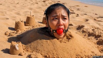 Close up of terrified Southeast Asian beauty with thick harness ball gag strapped in her mouth, eyes wide with fear 