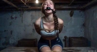 Distressed athletic sporty girl in gym clothes ballgagged and roped sitting on bench looking scared in dirty basement
