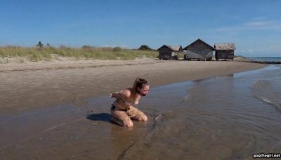 Wide shot of roped tourist girl on wooden table being carried through shallow surf by tribal men on remote island beach